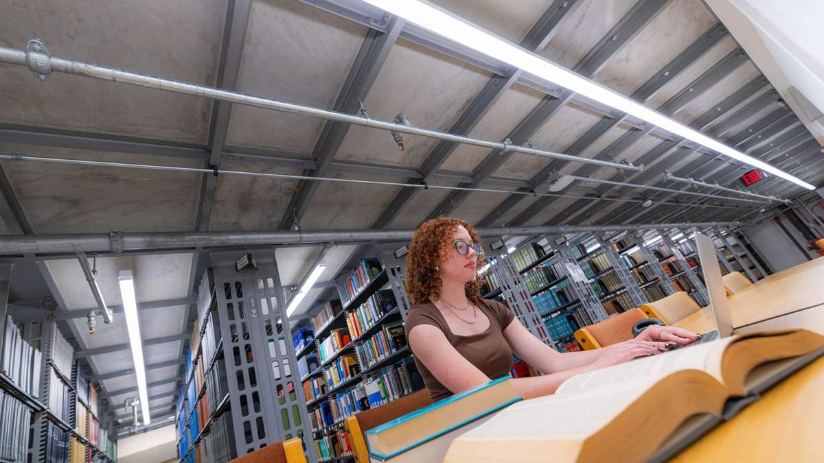 Female student with curly red hair studies near library shelves
